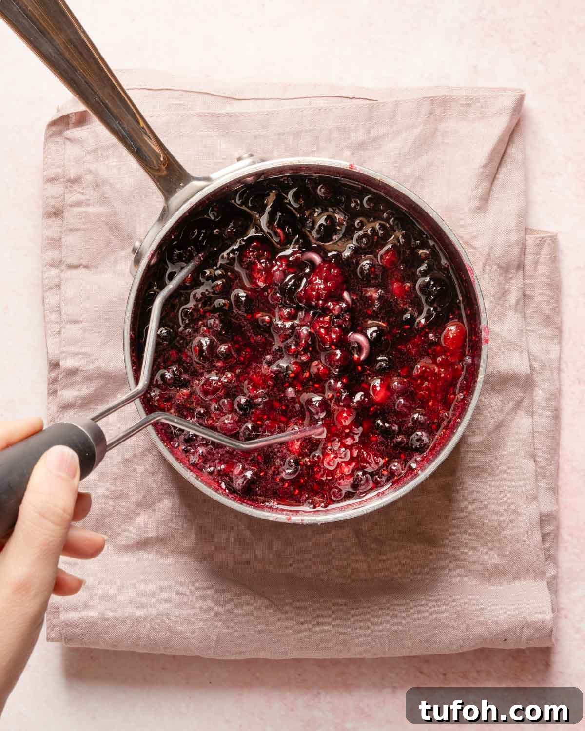 potato masher mashing cooked berries in a small pot.