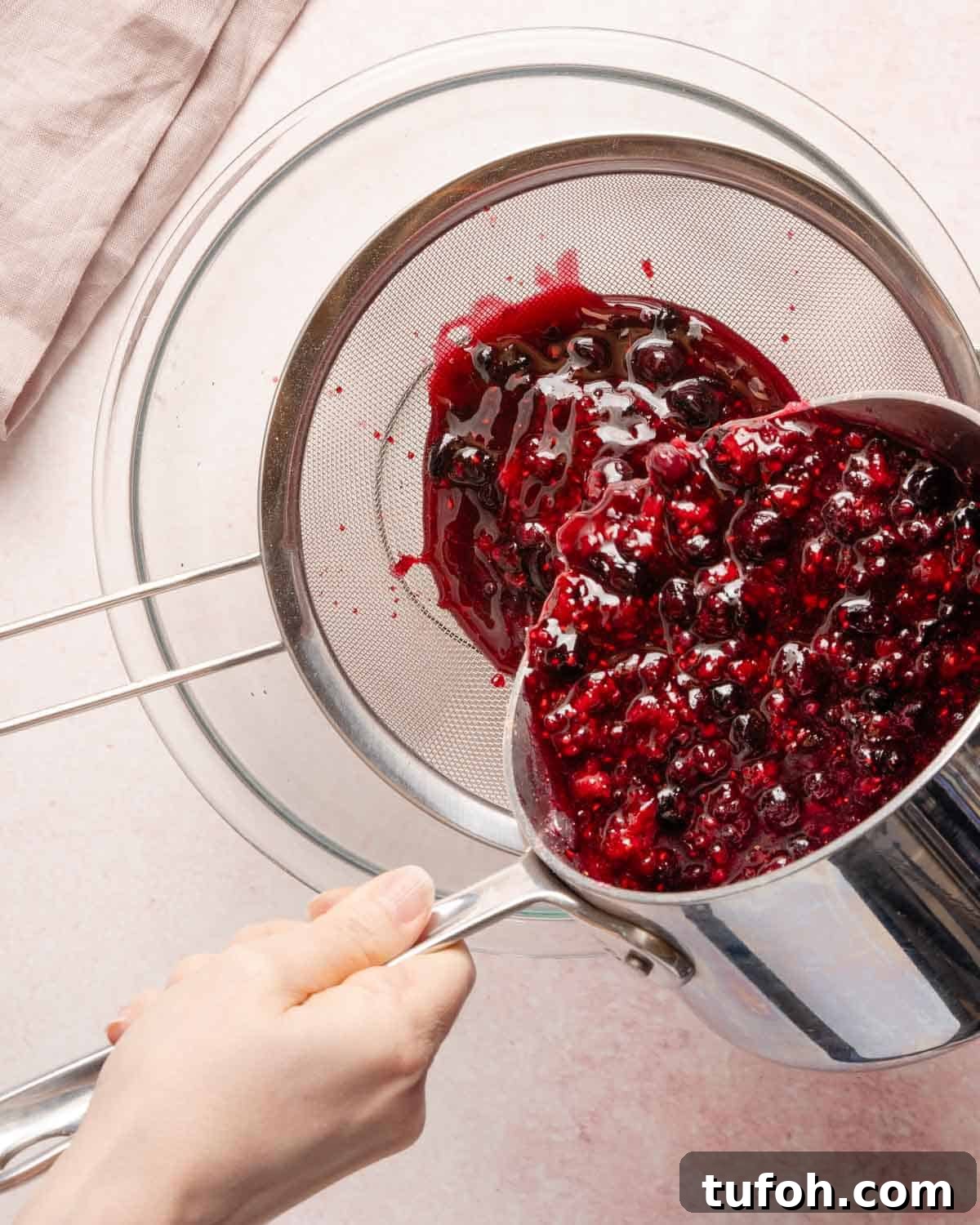 cooked berries being poured into a strainer set over a bowl.