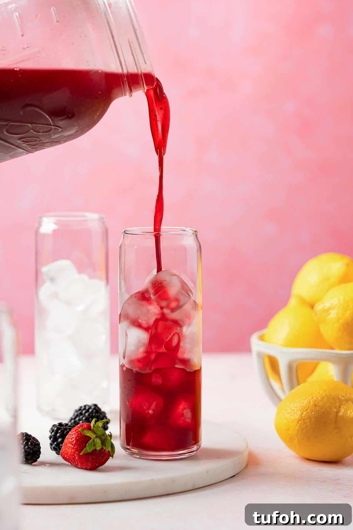 jug of berry lemonade being poured into a glass filled with ice.