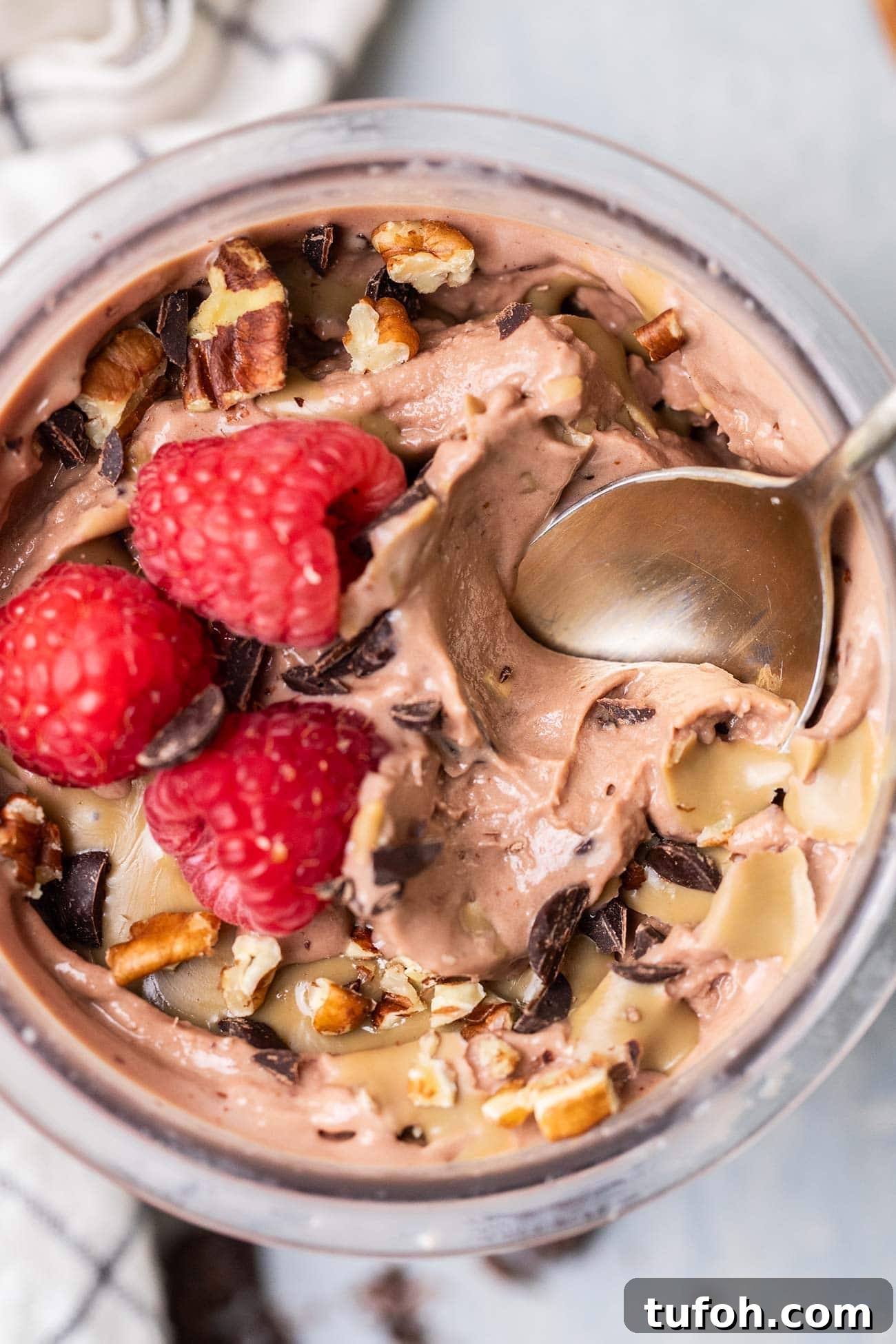 A top down view of a pint of thick chocolate protein ice cream topped with raspberries.