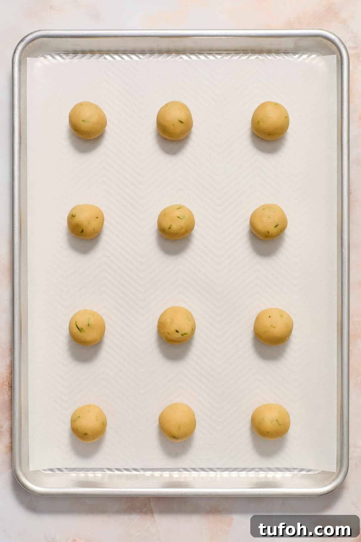 Key lime cookie dough rolled into balls on parchment lined baking sheet.