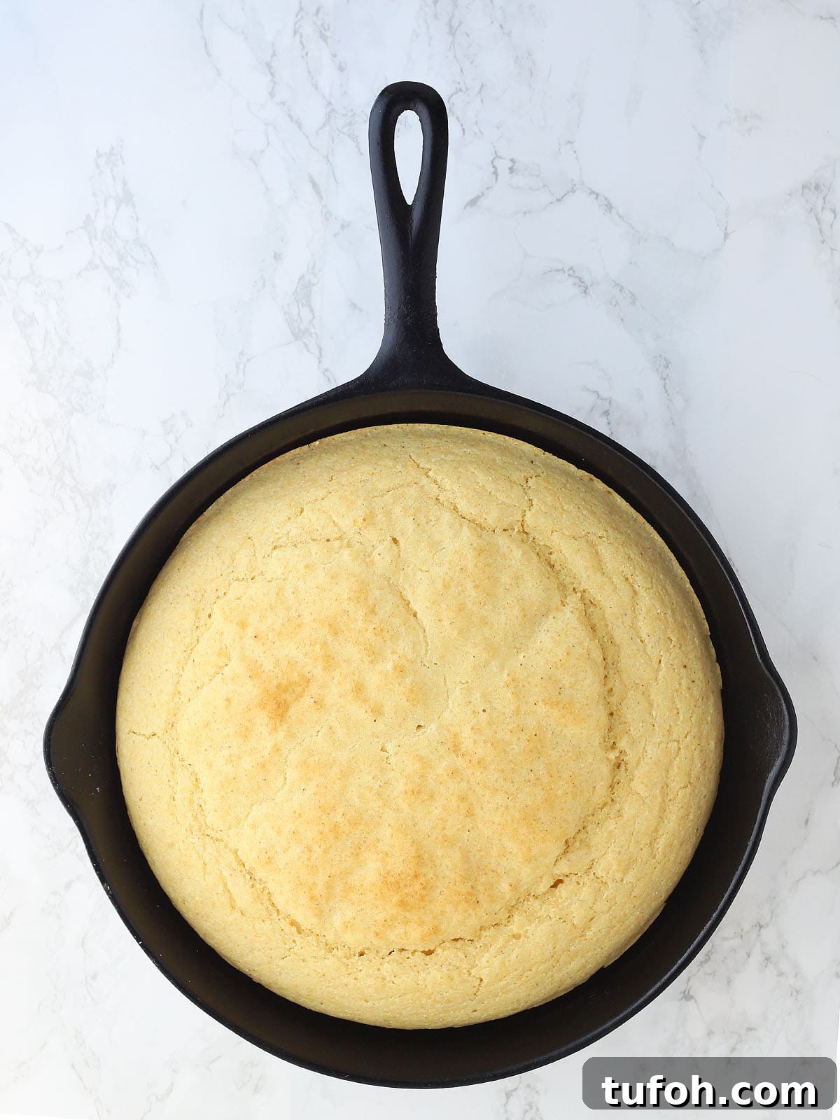 Baked cornbread in a cast iron skillet on a white background.