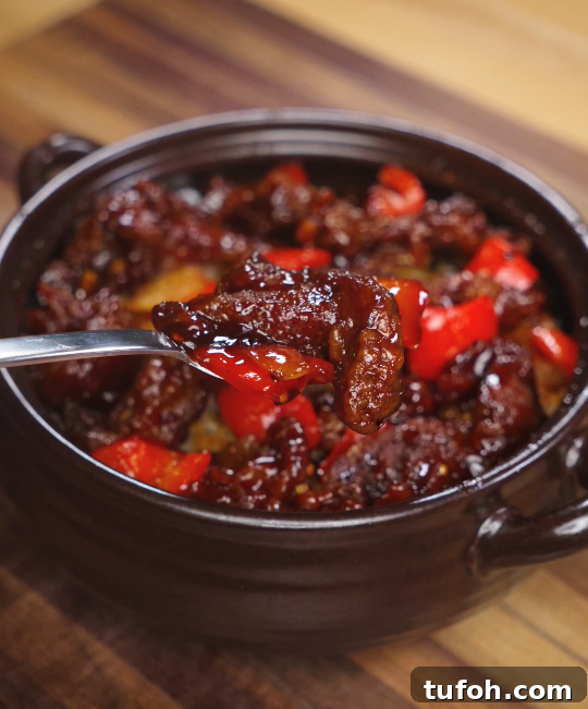 Beijing-Style Beef Stir-Fry Recipe 3 A fork lifting a glistening piece of Beijing Beef with red bell pepper from a bowl, showing crispy edges and rich sauce.