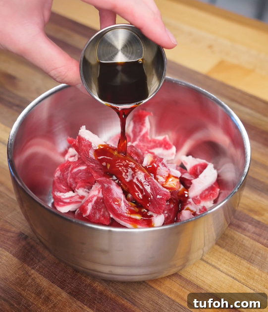Beijing-Style Beef Stir-Fry Recipe 4 Soy-based marinade being poured over raw sliced beef in a metal bowl, beginning the flavor-building step of Beijing Beef.