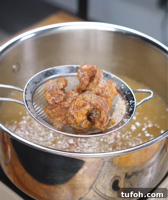 Beijing-Style Beef Stir-Fry Recipe 7 Golden brown crispy beef pieces resting in a skimmer above hot oil, fresh from deep frying for the Beijing Beef.