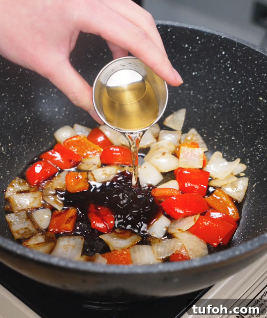 Beijing-Style Beef Stir-Fry Recipe 8 Chopped onions and red bell peppers sizzling in a wok as a hand pours vinegar into the glossy Beijing Beef sauce base.
