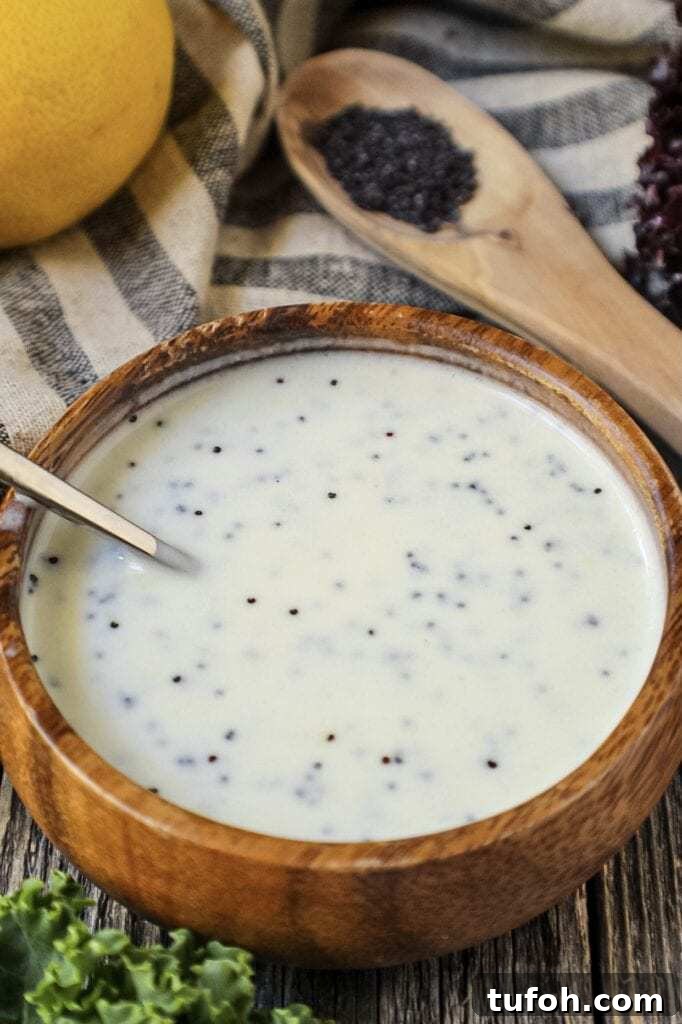 Creamy Lemon Poppyseed Salad Dressing Recipe 2 Creamy Lemon Poppyseed Dressing in a wooden bowl with wooden spoon filled with poppy seeds in shot along with a whole lemon, leaf lettuce and cloth napkin