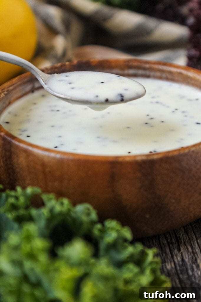 Creamy Lemon Poppyseed Salad Dressing Recipe 3 Creamy Lemon Poppyseed Dressing in a wooden bowl with wooden spoon filled with poppy seeds in shot along with a whole lemon, leaf lettuce and cloth napkin