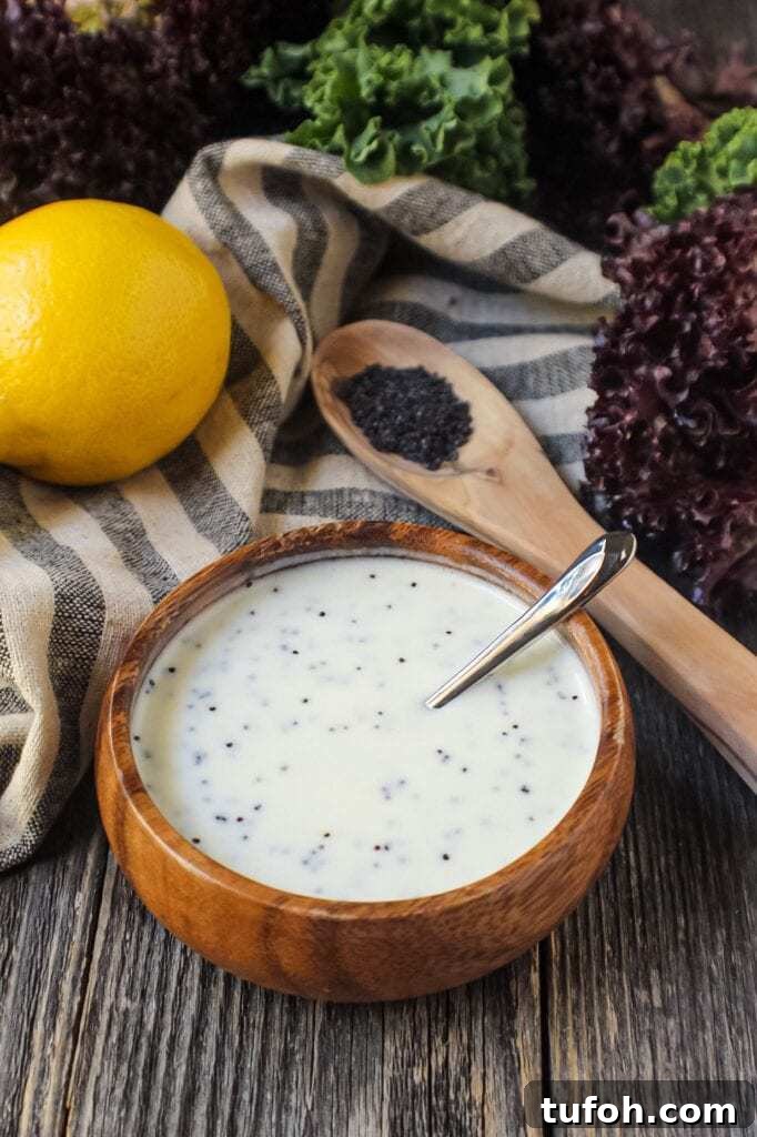 Creamy Lemon Poppyseed Salad Dressing Recipe 4 Creamy Lemon Poppyseed Dressing in a wooden bowl with wooden spoon filled with poppy seeds in shot along with a whole lemon, leaf lettuce and cloth napkin