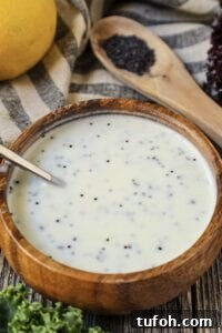 Creamy Lemon Poppyseed Salad Dressing Recipe 5 Creamy Lemon Poppyseed Dressing in a wooden bowl with wooden spoon filled with poppy seeds in shot along with a whole lemon, leaf lettuce and cloth napkin