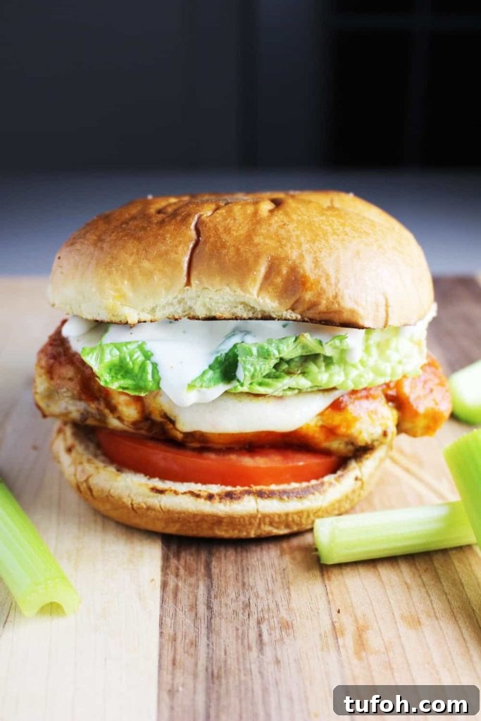 Buffalo Chicken Burgers with Tangy Blue Cheese Slaw 2 A Buffalo chicken burger topped with ranch dressing, tomato and lettuce on a wooden cutting board