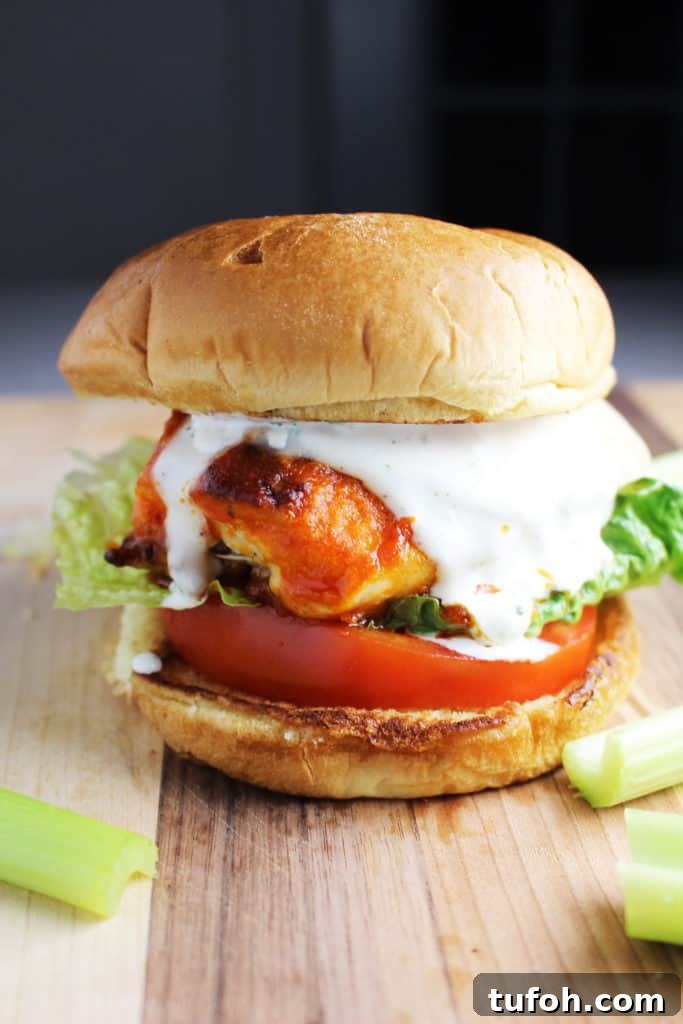 Buffalo Chicken Burgers with Tangy Blue Cheese Slaw 6 A Buffalo chicken burger with cheese, ranch, tomato and lettuce on a wooden cutting board