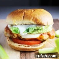 Buffalo Chicken Burgers with Tangy Blue Cheese Slaw 8 A Buffalo chicken burger with cheese, ranch, tomato and lettuce on a wooden cutting board