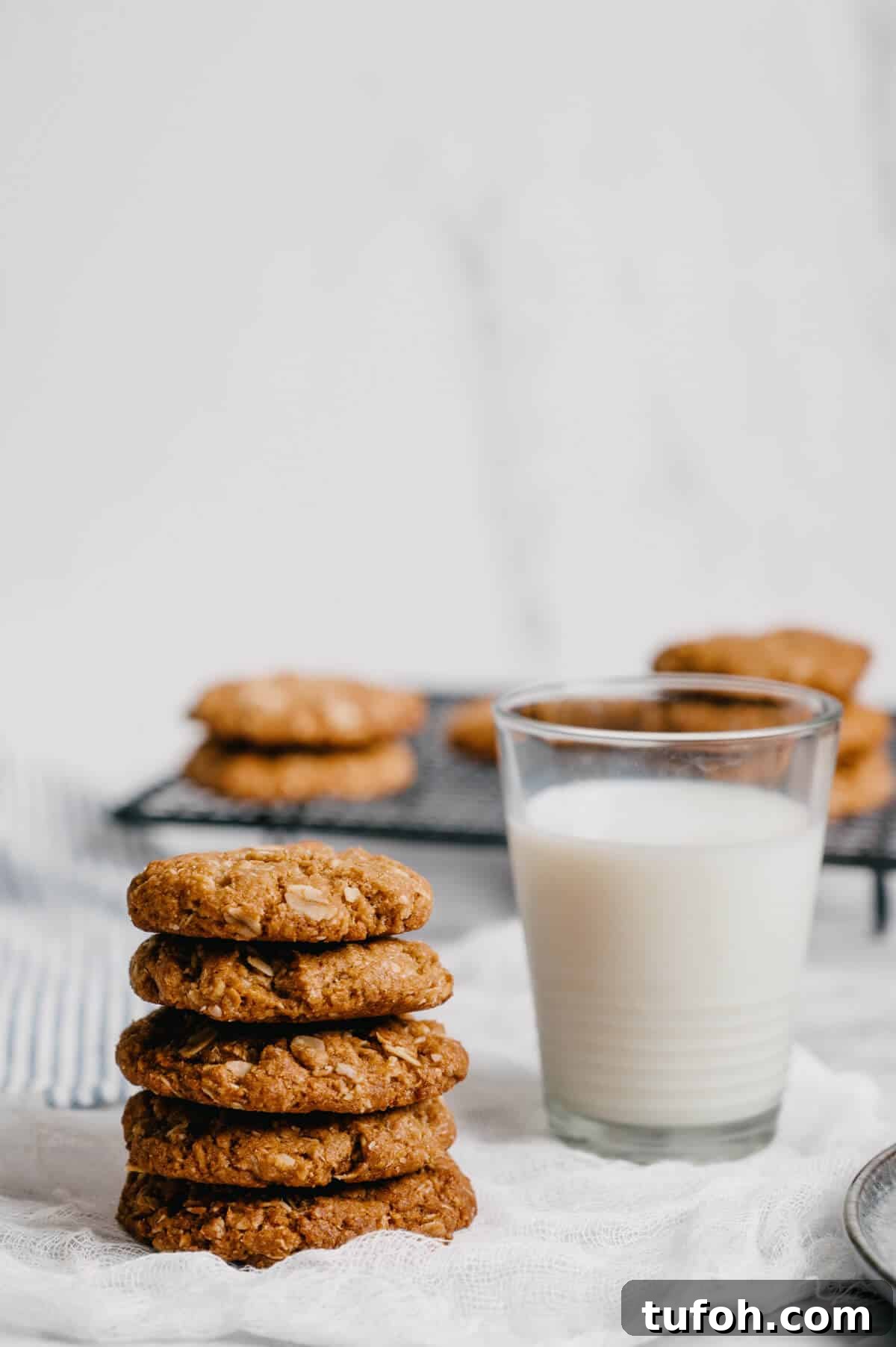 a stack of Anzac biscuits with a glass of milk next to them.