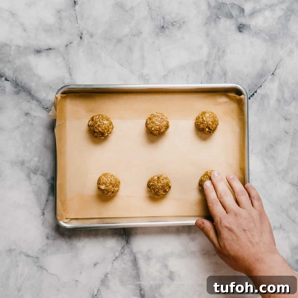 flattening unbaked Anzac biscuits on a baking tray.