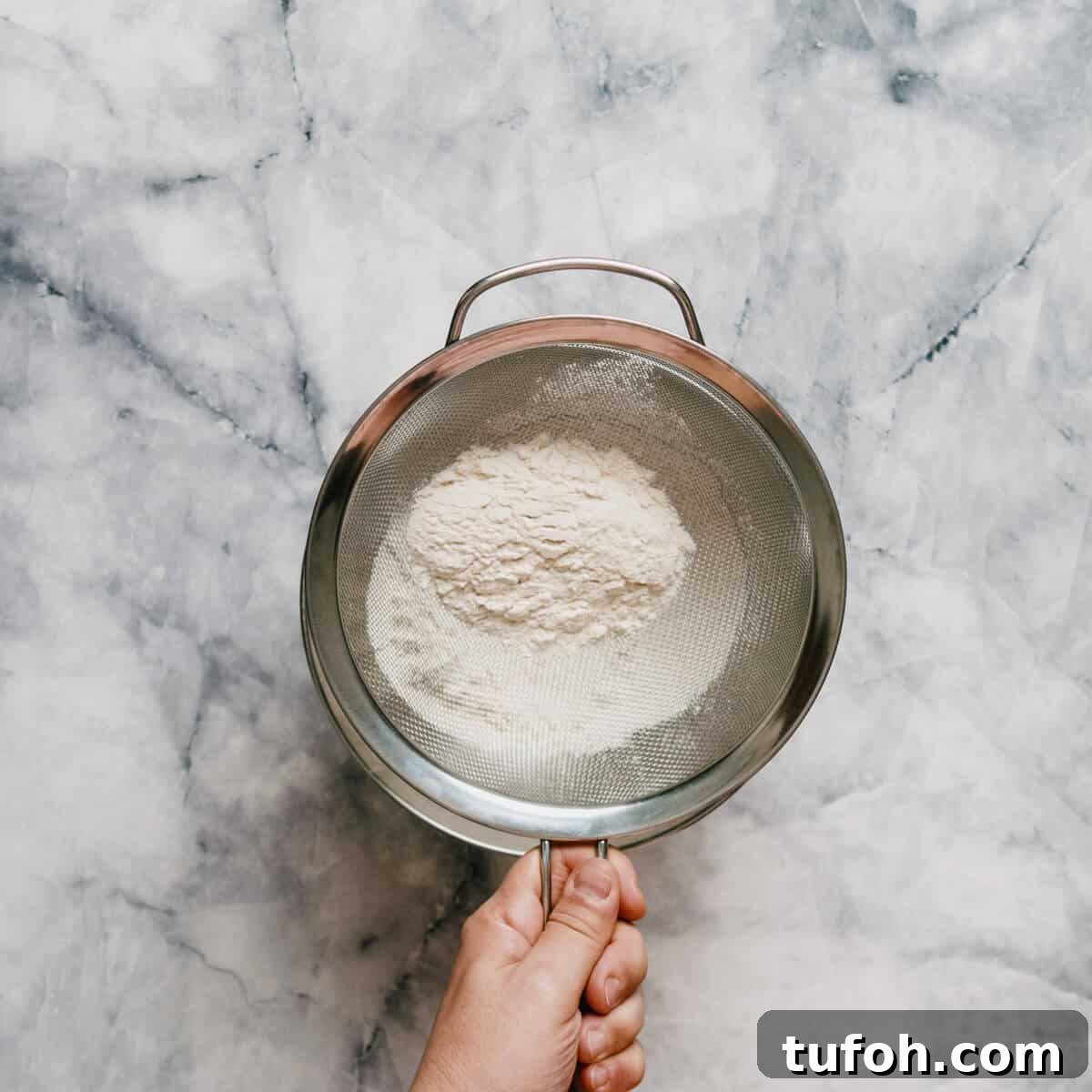 sifting flour into a stainless steel bowl.