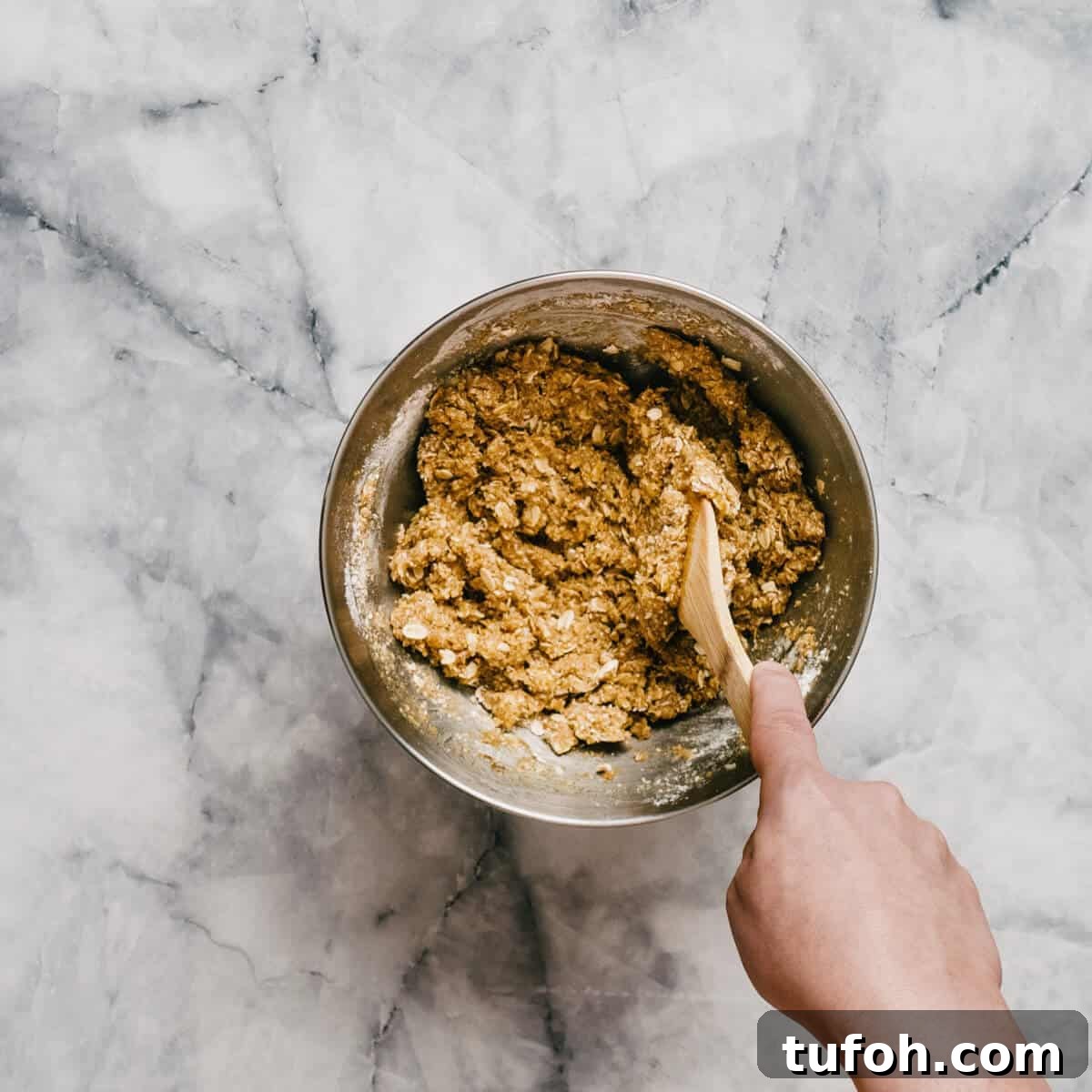 mixing Anzac cookie dough in a stainless steel bowl.
