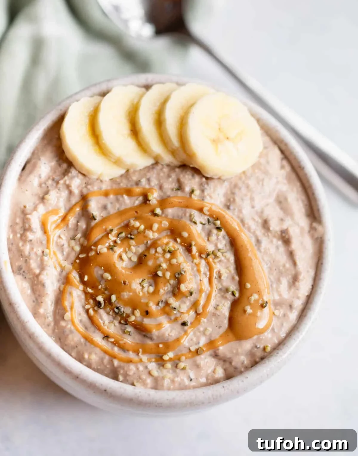 Peanut Butter Chocolate Overnight Oats Recipe for Creamy Mornings 2 Peanut Butter Chocolate Blended Overnight Oats in a speckled bowl topped with sliced bananas, a drizzle of peanut butter, and hemp seed hearts.