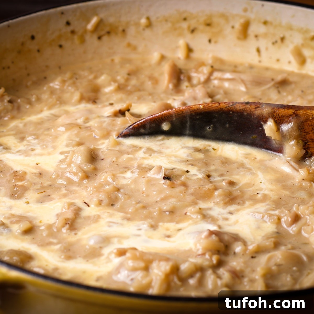 Creamy Mushroom Chicken with Parmesan Rice Bowl 12 Someone using a wooden spoon to stir egg yolks and cream into chicken and rice.