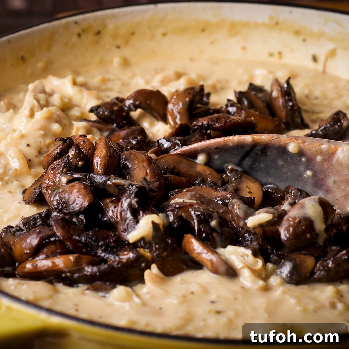 Creamy Mushroom Chicken with Parmesan Rice Bowl 13 Someone using a wooden spoon to stir caramelized mushrooms into a pan of creamy chicken and rice.