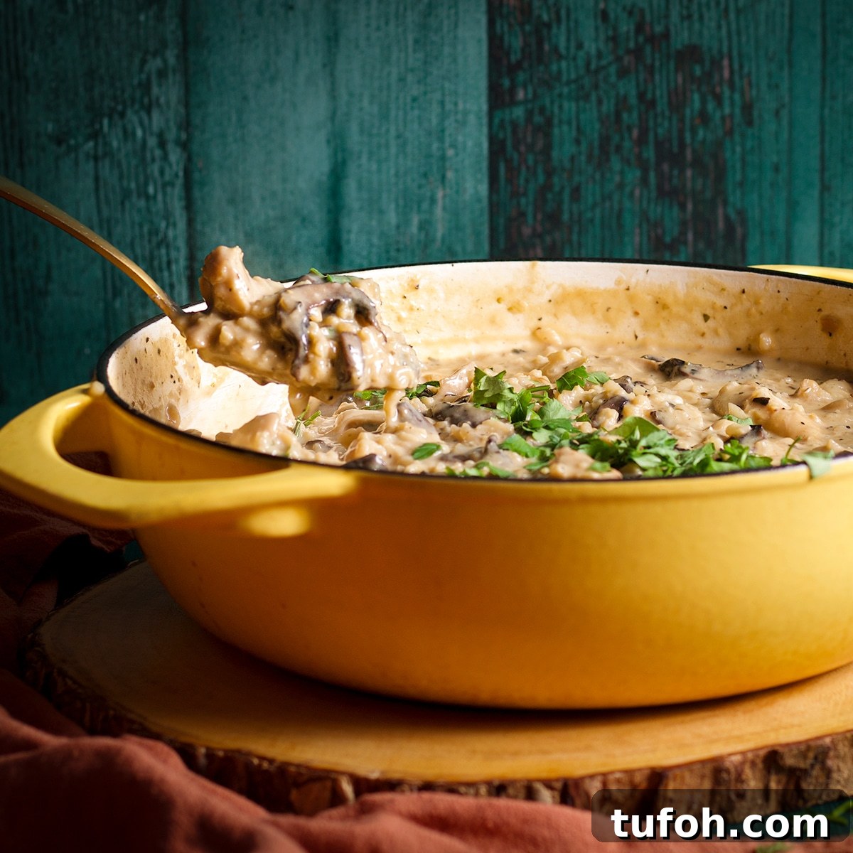 Creamy Mushroom Chicken with Parmesan Rice Bowl 16 Someone lifting a spoonful of creamy mushroom chicken and rice from a large sauce pan.