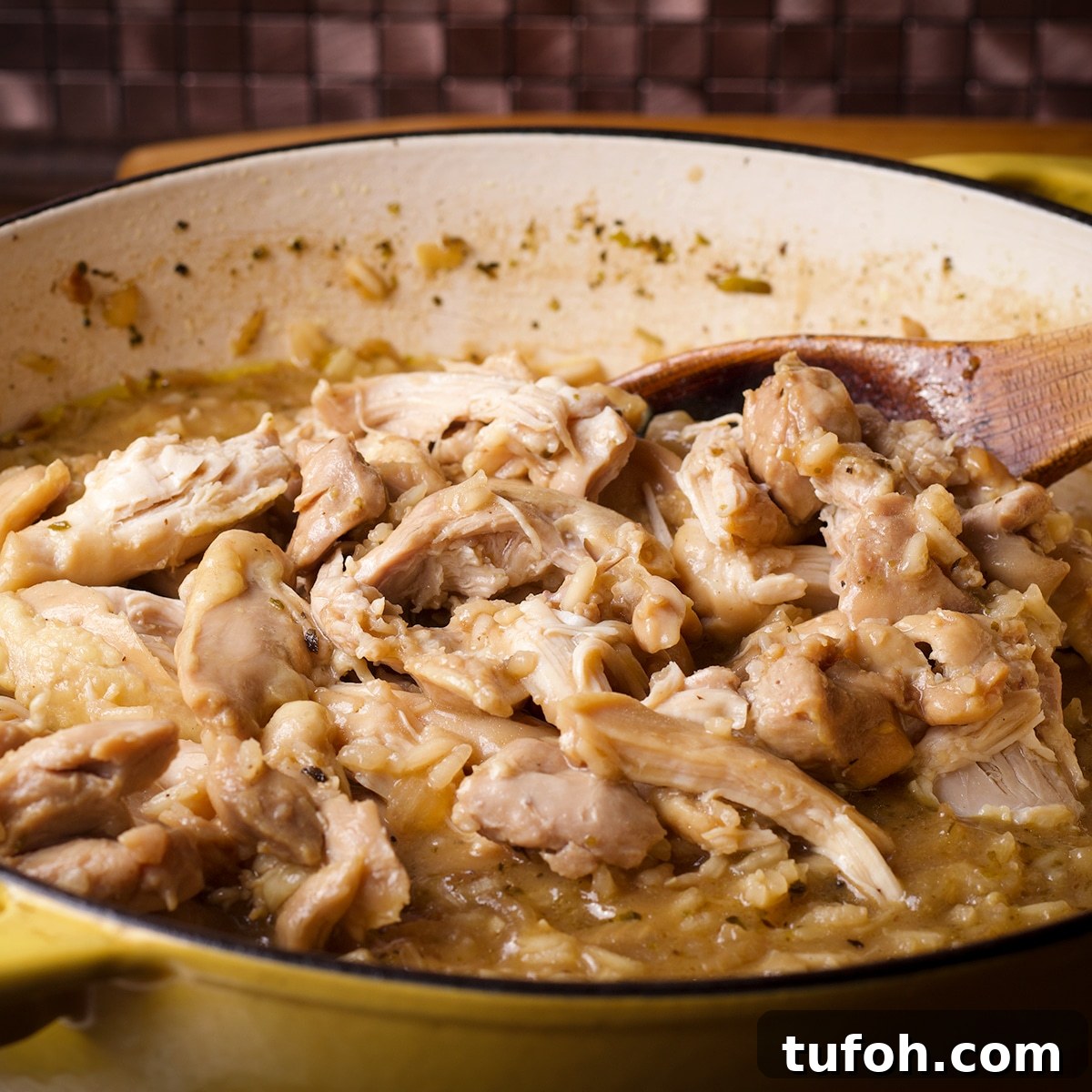 Creamy Mushroom Chicken with Parmesan Rice Bowl 10 Someone using a wooden spoon to stir shredded cooked chicken back into the sauce pan with rice.