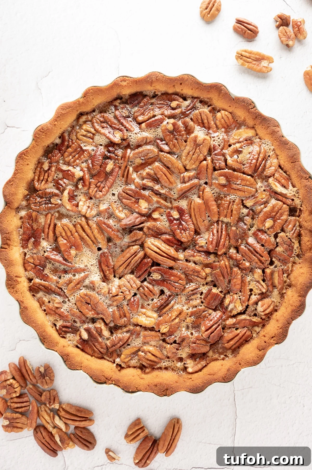 sugar-free pecan pie on a bright white back ground with scattered raw pecans. 
