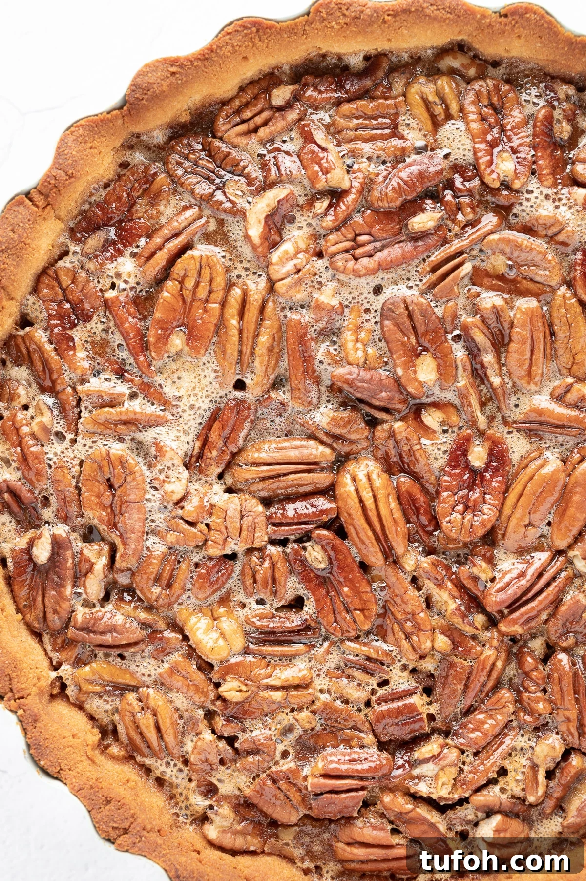 a close up image of the top of a pecan pie showing the sticky gooey texture of the filling and golden baked pecans in a perfectly baked crust. 