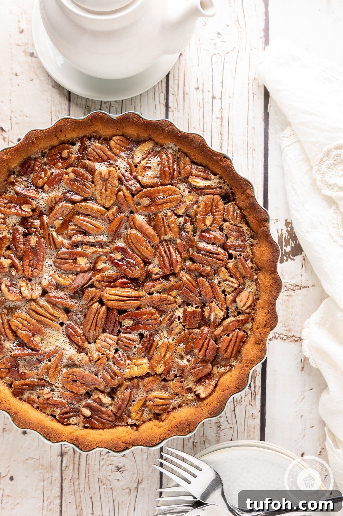 Pecan pie on a rustic wooden backdrop with white napkin, plates and a pot of hot tea