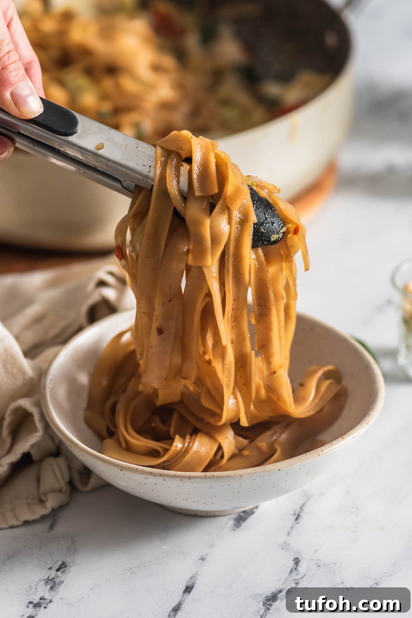 Vegan Drunken Noodles Recipe — Spicy Thai Stir-Fry 2 Using tongs to scoop a serving of Thai drunken noodles into a small bowl.