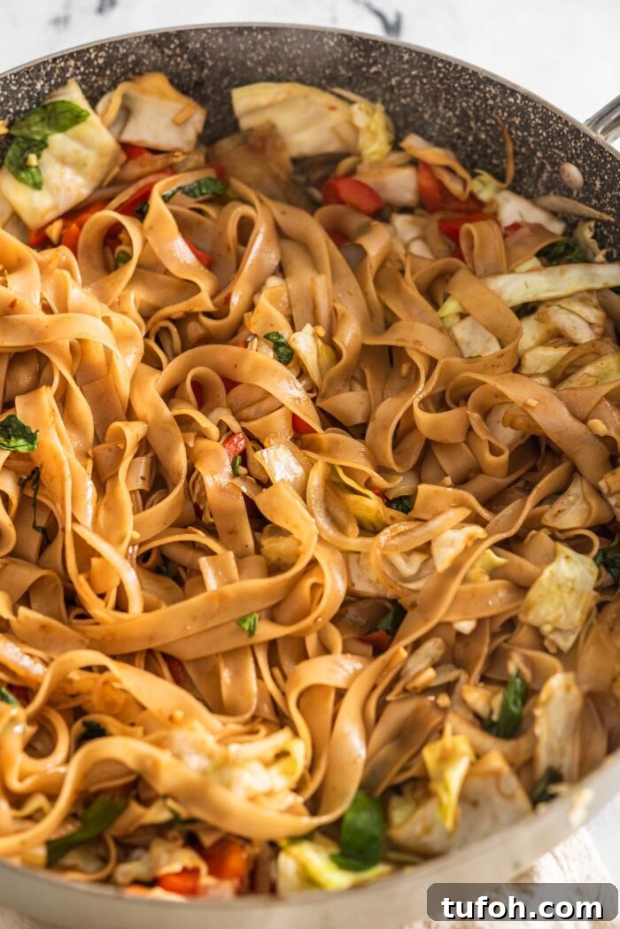 Vegan Drunken Noodles Recipe — Spicy Thai Stir-Fry 8 Overhead view of a large pan of vegan drunken noodles with cabbage, onion, bell pepper and green onion.