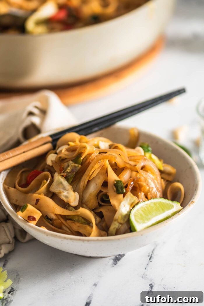 Vegan Drunken Noodles Recipe — Spicy Thai Stir-Fry 9 Pair of chopsticks resting on a bowl of vegan drunken noodles with a wedge of lime resting in the bowl.
