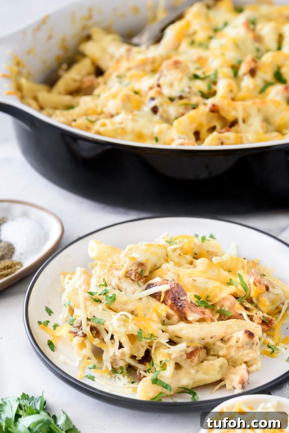 A plate with a portion of chicken alfredo casserole. A casserole dish with the remaining casserole is next to the plate.