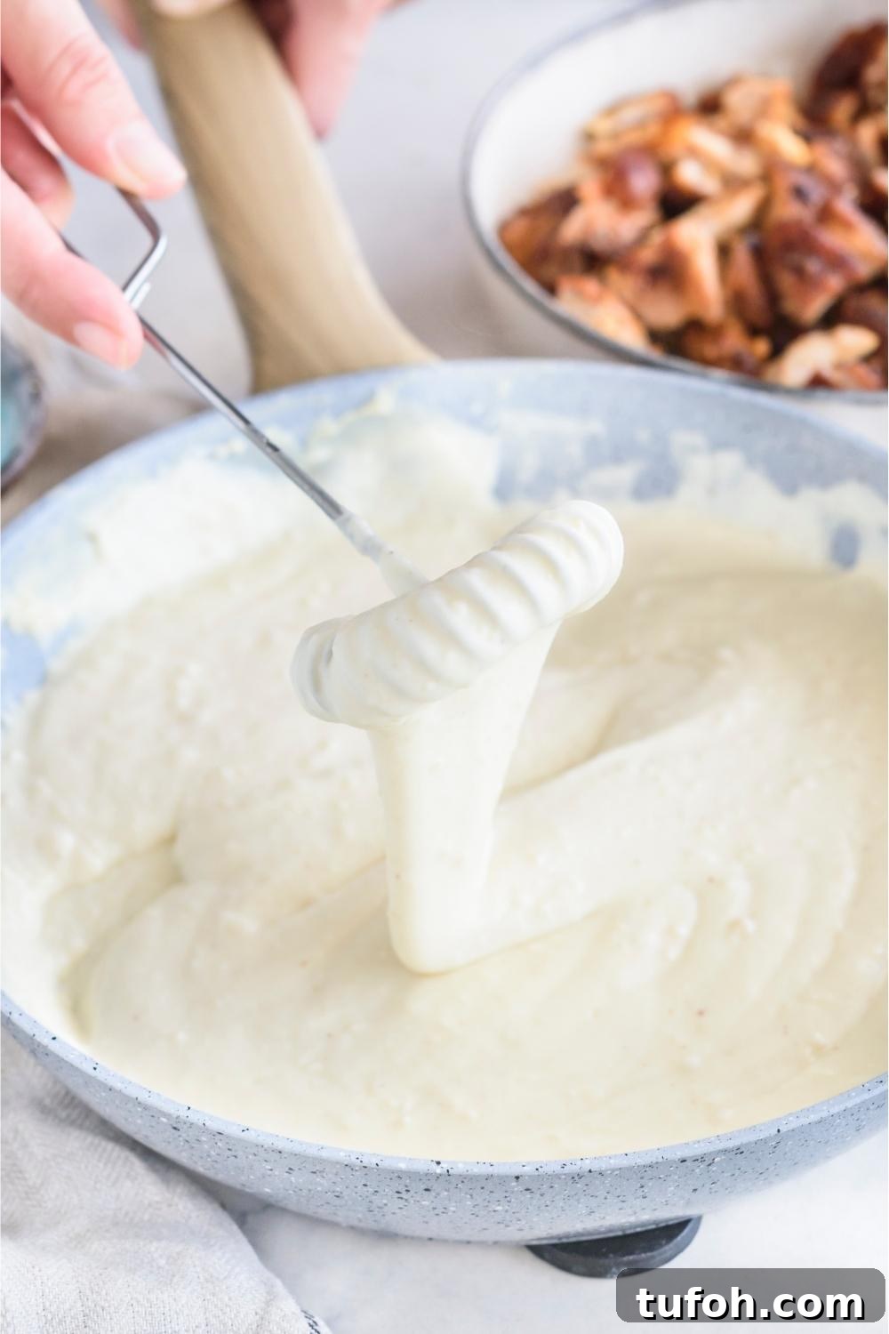 A skillet with creamy alfredo sauce being mixed.
