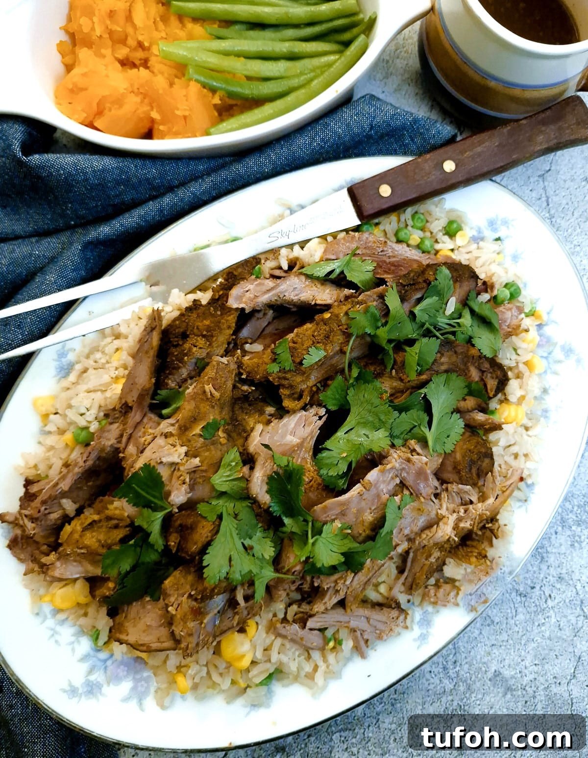 Slow-Cooked Curried Leg of Lamb in Foil for Tender Flavor 11 Overhead shot of a serving plate with sliced lamb on a bed of rice garnished with fresh coriander leaves.