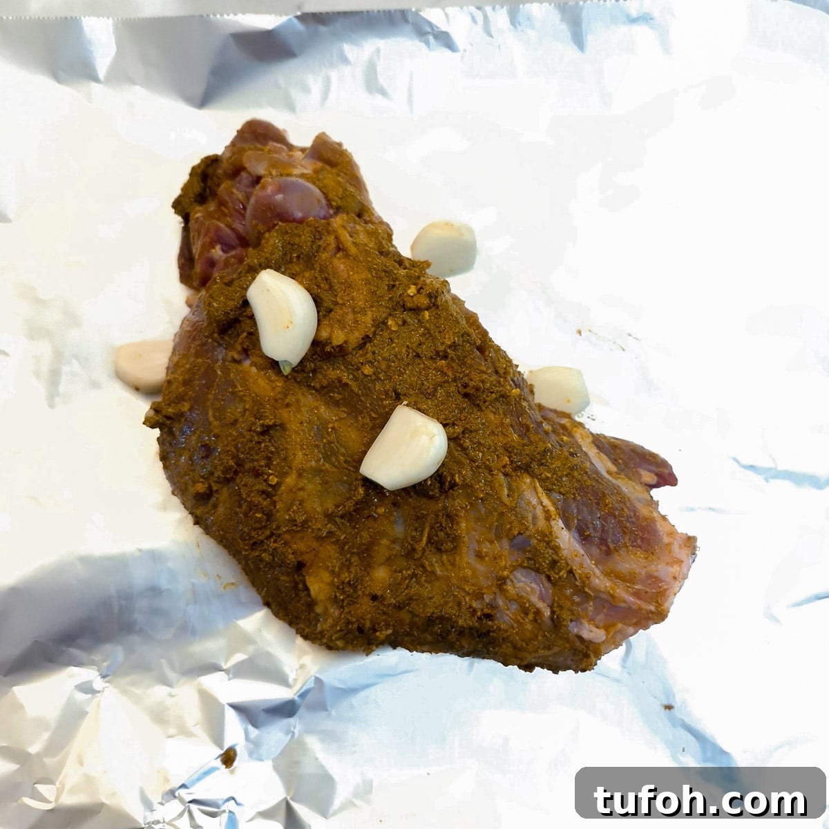 Slow-Cooked Curried Leg of Lamb in Foil for Tender Flavor 7 Curry coated leg of lam on a sheet of tin foil with cloves of garlic.