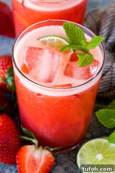 A glass of strawberry agua fresca garnished with mint and lime.