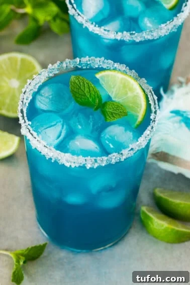 Two cups of blue margarita with a sugared rim and lime wedge for garnish.