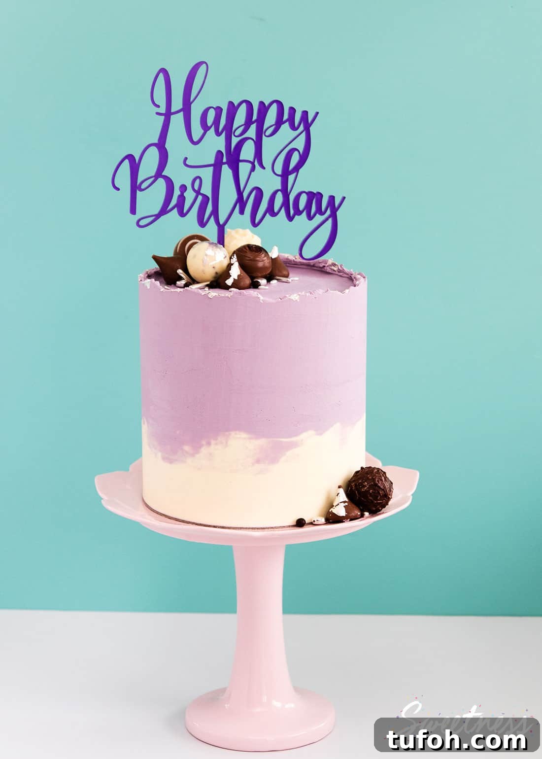How to Make a Rough-Edge Ganache Drip Cake: Step-by-Step Tutorial 6 A cake covered in purple and white swirled ganache with a rough top edge, decorated with chocolates and a happy birthday acrylic topper.