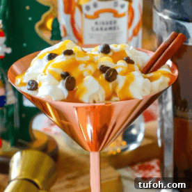 A copper martini glass brimming with whipped cream, caramel sauce, coffee beans, and cinnamon sticks