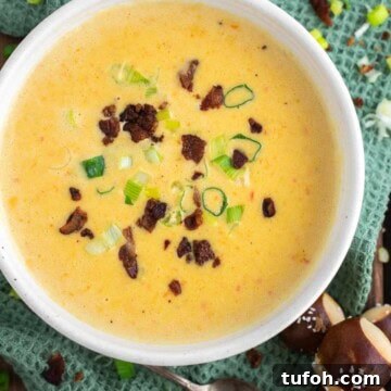 Beer cheese soup in bowl with bacon and scallions on dish towel.