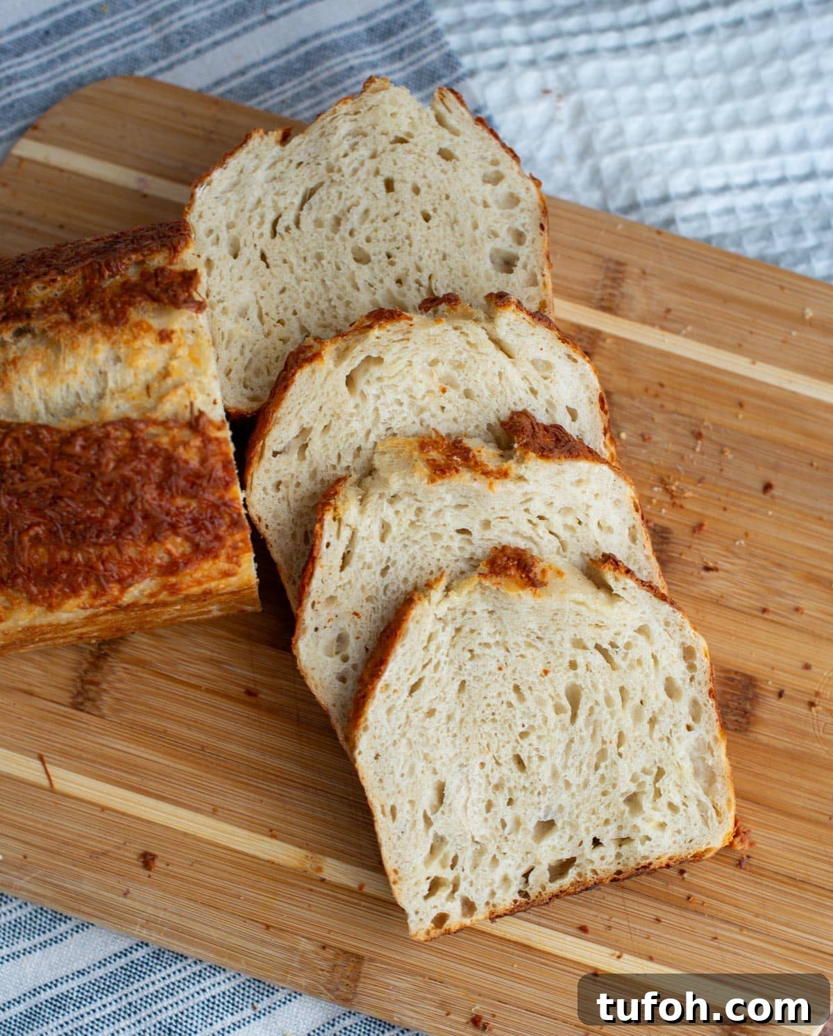 Asiago Sourdough Bagel Loaf Recipe: Chewy Crust, Tangy Interior 11 Four slices of sourdough bagel bread are sliced on a wooden cutting board.