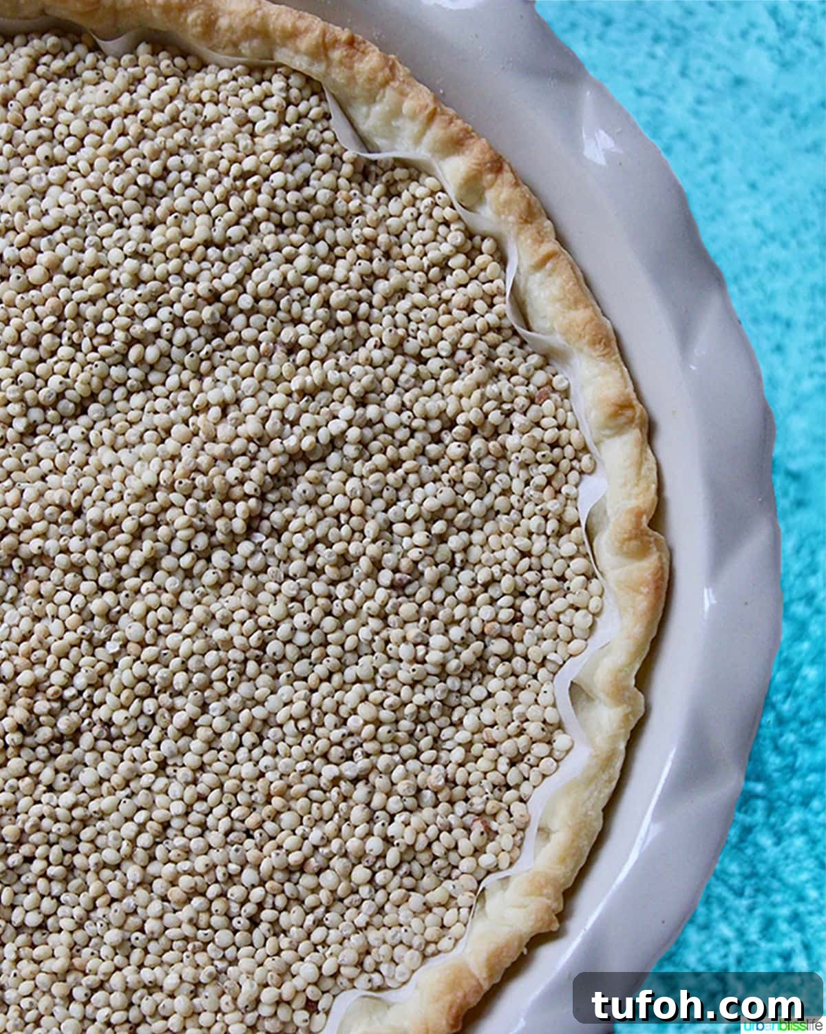 Decadent Chocolate Bourbon Pecan Pie Recipe 4 pie crust with pie weights in a pie pan on blue table.