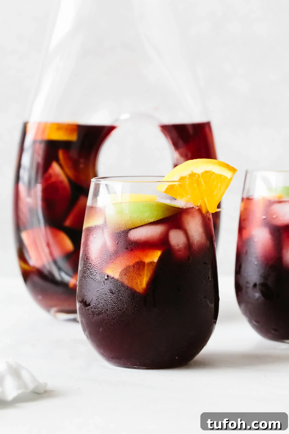25+ Memorial Day Recipes for Grilling, Picnics & Desserts 6 Red sangria in a glass with orange slice garnish and pitcher in the background.