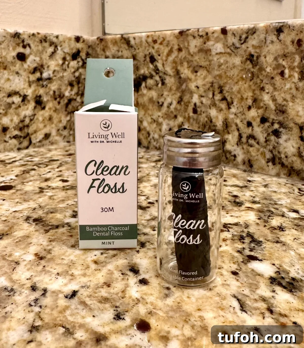Non-Toxic Natural Dental Floss Without PFAS — Top Picks 14 Living Well ‘Clean Floss’ box and a refillable glass jar holding black bamboo charcoal dental floss displayed on a granite countertop.