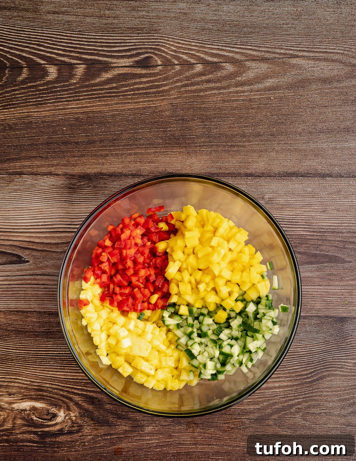 Tangy Pineapple Mango Salsa Recipe for Grilled Fish & Tacos 9 a bowl with diced mango, cucumber, pineapple, and red bell pepper in it.
