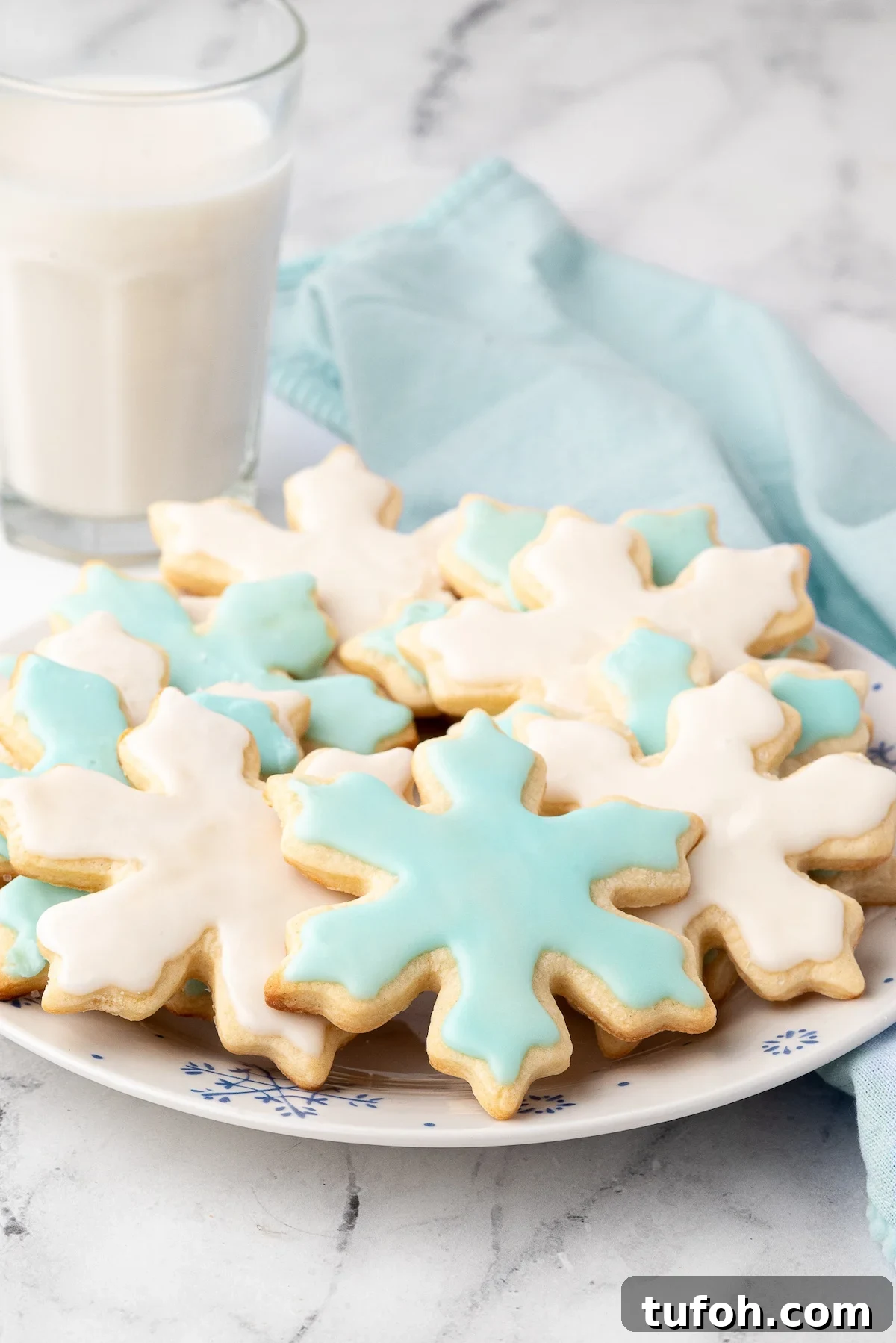 Soft Cut-Out Sugar Cookies Recipe for Tender, Perfect Shapes 12 Snowflake sugar cookies decorated with white and light blue icing.