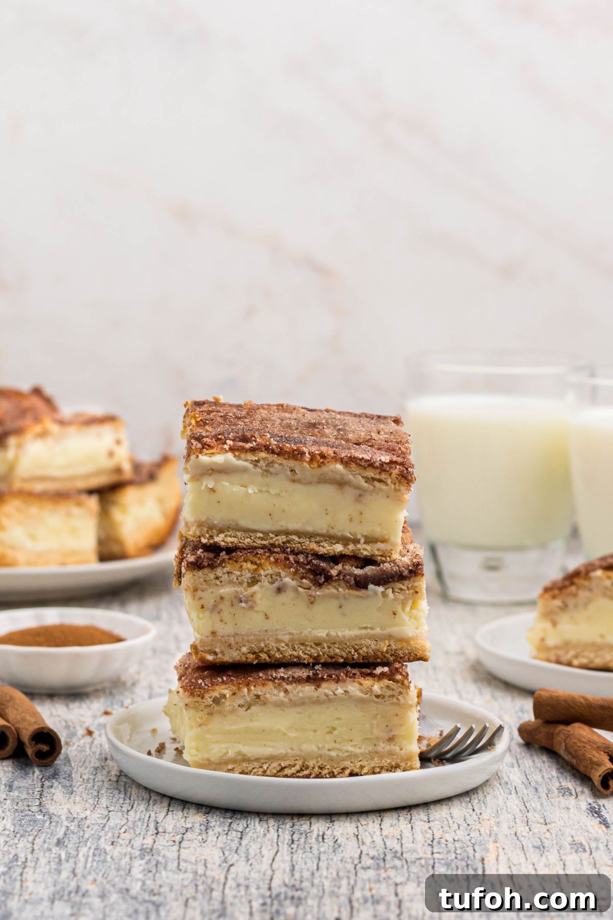 Churro Cheesecake Recipe: Cinnamon-Sugar Cheesecake Bars 11 Three slices of cheesecake, stacked on a small white plate in front of glasses of milk.