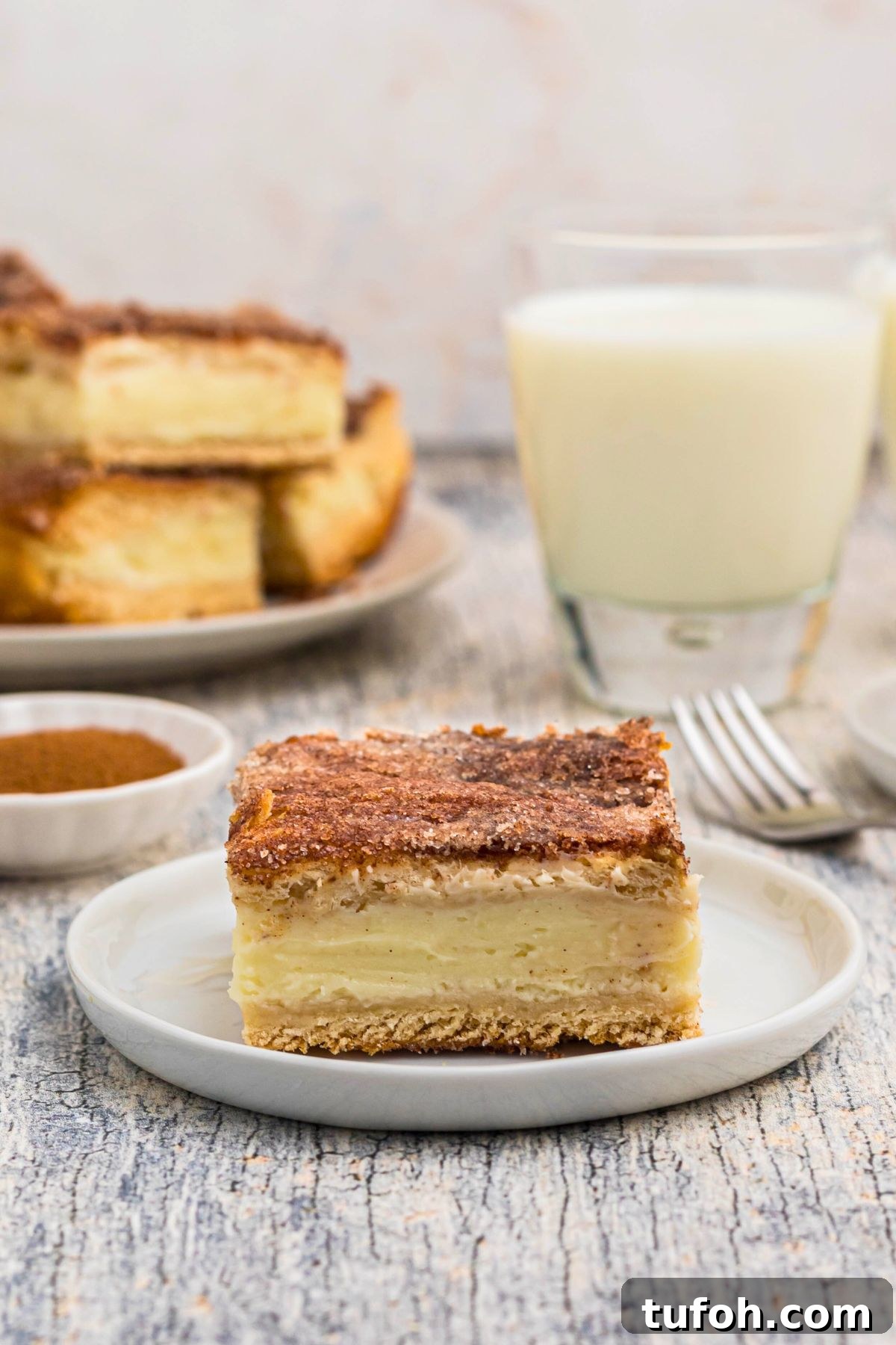 Churro Cheesecake Recipe: Cinnamon-Sugar Cheesecake Bars 12 Slice of churro cheesecake served on a small white plate in front of glasses of milk.