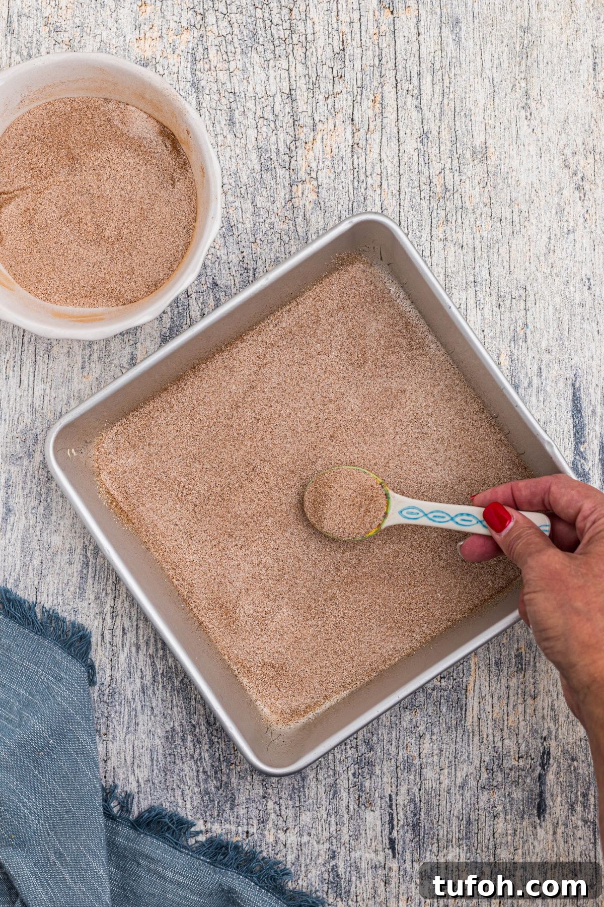 Churro Cheesecake Recipe: Cinnamon-Sugar Cheesecake Bars 4 Sugar and cinnamon mixture being added to bottom of square pan.